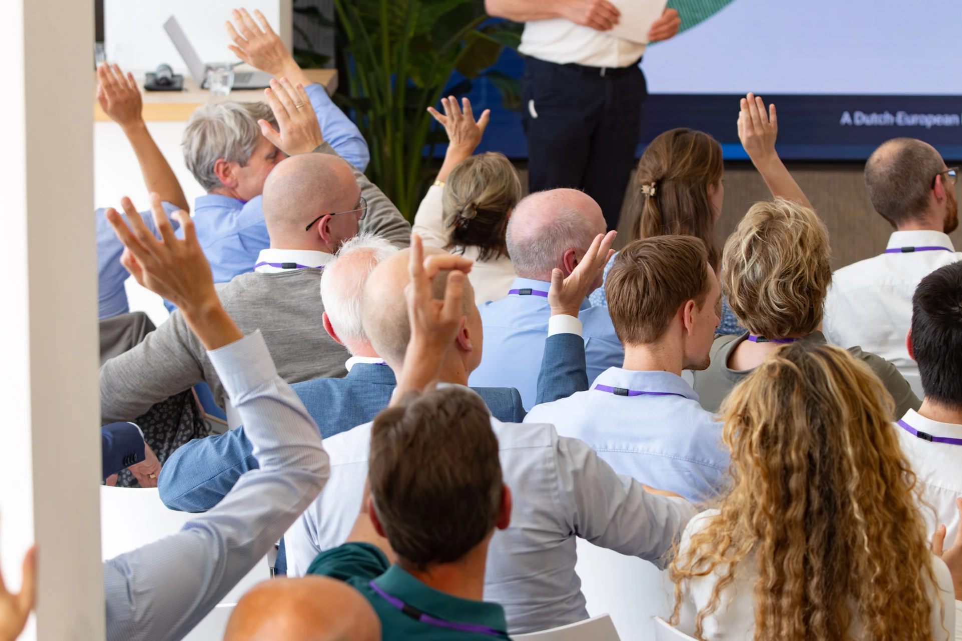 Audience members raise their hands at the EUH2STARS consortium plenary meeting in Utrecht, photographed from behind